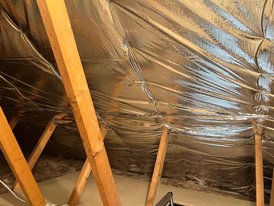 Multifoil insulation fixed across the rafters of a Scottish loft, with mineral wool still laid at the loft floor below