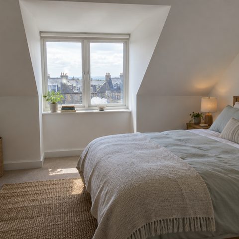 A finished loft conversion bedroom with sloping coombed ceilings and a dormer window.