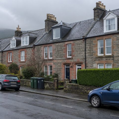 A terrace of Scottish sandstone houses with slate roofs, dormer windows and chimney stacks on an overcast day.